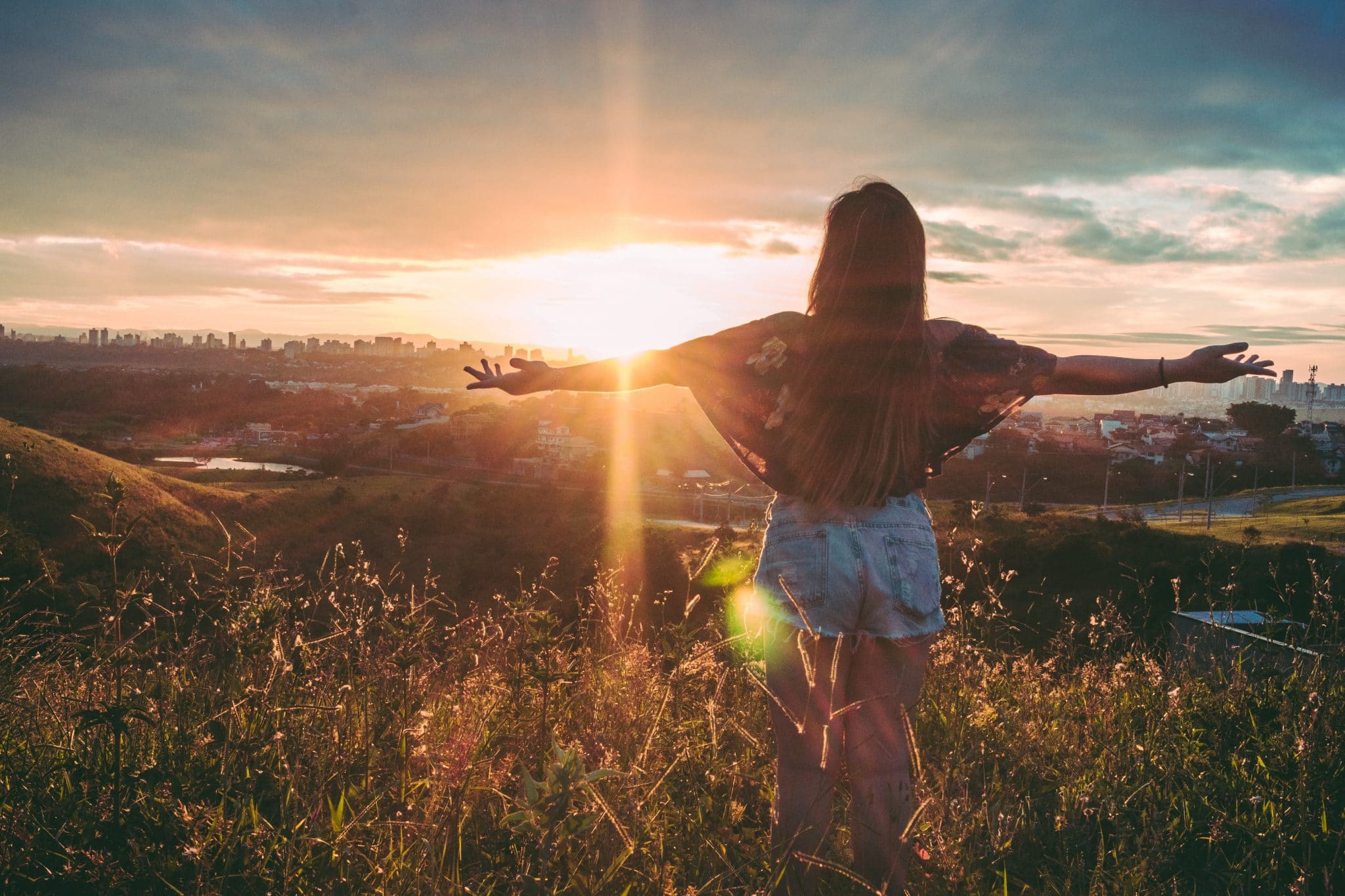 woman-stands-on-mountain-over-field-under-cloudy-sky-at-847483
